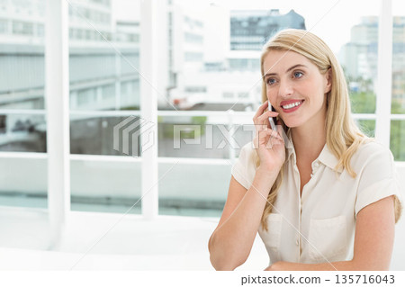 Woman wearing short-sleeve blouse sitting at white desk by window, holding smartphone, copy space Woman wearing short-sleeve blouse sitting at white desk by window, holding smartphone, copy space 135716043