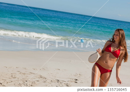 Woman wearing red bikini playing with blue ball on sandy beach with wooden paddle, copy space Woman wearing red bikini playing with blue ball on sandy beach with wooden paddle, copy space 135716045