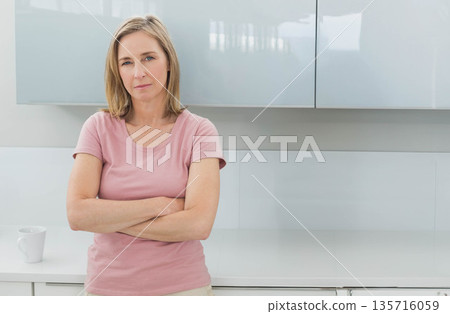 Mature woman standing in modern kitchen with glossy cabinets wearing pink T-shirt near white mug 135716059