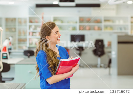 Woman in blue scrub top holding red notebook and pink folder in clinical lab, copy space 135716072