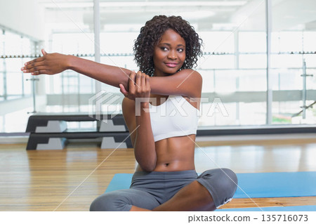 African American woman stretching on blue mat in gym wearing white-bra gray-leggings by glass wall African American woman stretching on blue mat in gym wearing white-bra gray-leggings by glass wall 135716073
