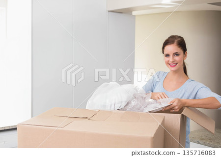 Adult female removing pillow in bubble wrap from cardboard box on kitchen island wearing blue top Adult female removing pillow in bubble wrap from cardboard box on kitchen island wearing blue top 135716083