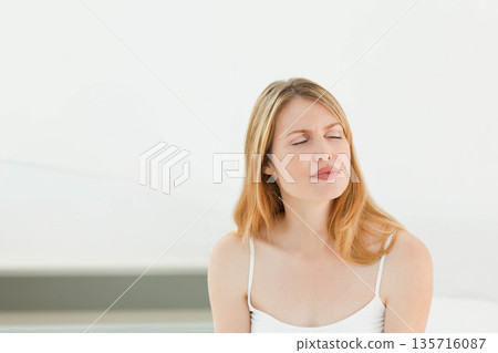 Mid-adult female sitting in bright studio wearing strappy top, pale ledge, eyes closed, copy space Mid-adult female sitting in bright studio wearing strappy top, pale ledge, eyes closed, copy space 135716087