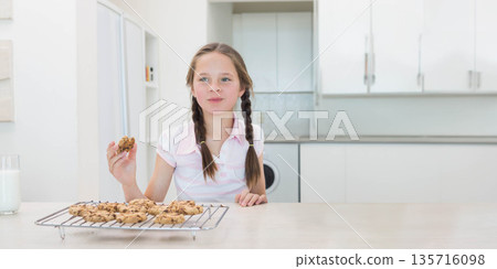 Girl child sitting at kitchen counter holding cookie, wearing pink shirt, cooling rack and milk Girl child sitting at kitchen counter holding cookie, wearing pink shirt, cooling rack and milk 135716098