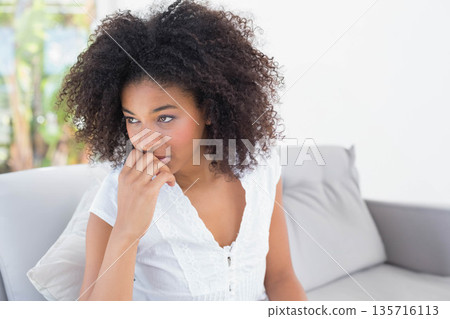 African American woman in twenties sitting on sofa in living room, wearing white lace blouse 135716113