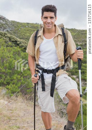 Adult male hiker standing on rocky trail, holding trekking poles, wearing beige shirt and backpack Adult male hiker standing on rocky trail, holding trekking poles, wearing beige shirt and backpack 135716115
