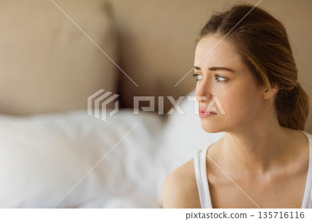 Woman in late twenties sitting on bed facing right, wearing white tank top, pensive, copy space Woman in late twenties sitting on bed facing right, wearing white tank top, pensive, copy space 135716116
