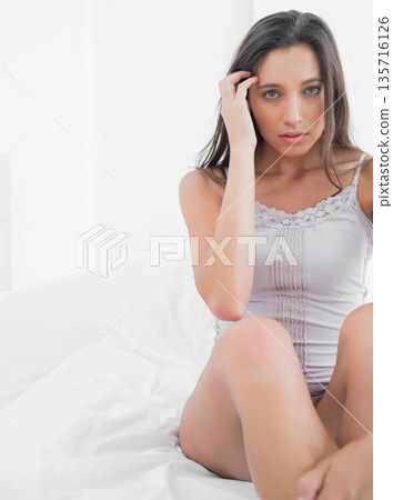 Adult female sitting on white bed touching hair and looking at camera, camisole, copy space Adult female sitting on white bed touching hair and looking at camera, camisole, copy space 135716126