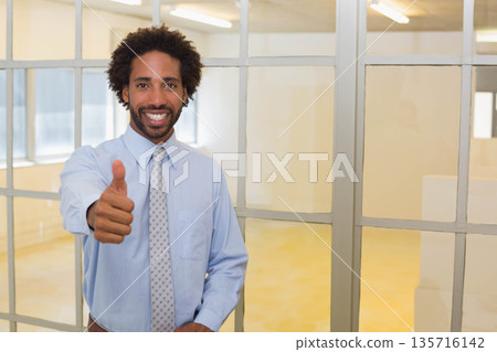 African American man in shirt and tie standing by metal-framed glass partition giving thumbs up 135716142