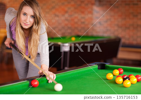 Woman in twenties leaning over pool table in pool hall, aiming cue at white cue ball 135716153