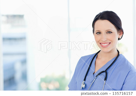 Adult woman clinician standing on right near window wearing blue scrubs and stethoscope, copy space Adult woman clinician standing on right near window wearing blue scrubs and stethoscope, copy space 135716157