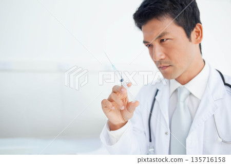 Asian male doctor in clinic white coat stethoscope holding syringe checking needle, copy space Asian male doctor in clinic white coat stethoscope holding syringe checking needle, copy space 135716158