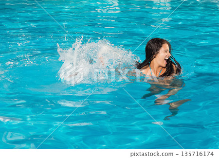 Woman kicking and splashing in turquoise pool, blue swimsuit straps visible, copy space Woman kicking and splashing in turquoise pool, blue swimsuit straps visible, copy space 135716174