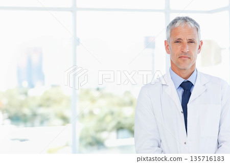 Senior doctor standing right by large glass windows, wearing white coat and dark tie, copy space Senior doctor standing right by large glass windows, wearing white coat and dark tie, copy space 135716183