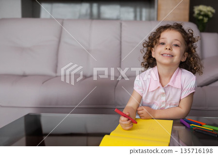 Female child drawing red marker on yellow pad at glass-top table in living room, copy space 135716198