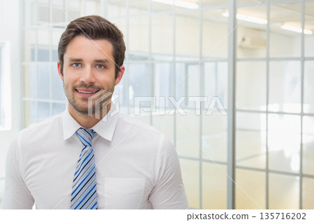 Man in his 30s standing in office with glass partitions wearing white shirt blue-striped tie Man in his 30s standing in office with glass partitions wearing white shirt blue-striped tie 135716202