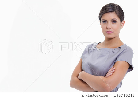 Woman standing with arms folded, facing camera in white studio wearing grey dress, copy space Woman standing with arms folded, facing camera in white studio wearing grey dress, copy space 135716215