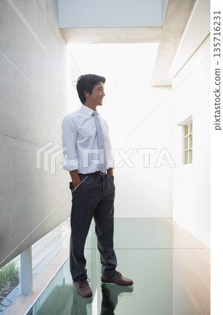 Mid-adult Asian man standing in modern atrium on glass floor, wearing white shirt, patterned tie Mid-adult Asian man standing in modern atrium on glass floor, wearing white shirt, patterned tie 135716231