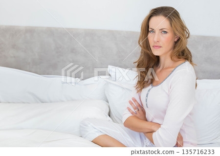 Woman sitting on bed in softly lit bedroom, wearing pajamas and showing ring, copy space Woman sitting on bed in softly lit bedroom, wearing pajamas and showing ring, copy space 135716233