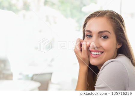 Woman smiling, resting hand against cheek at cafe near blurred tables and windows, copy space 135716239
