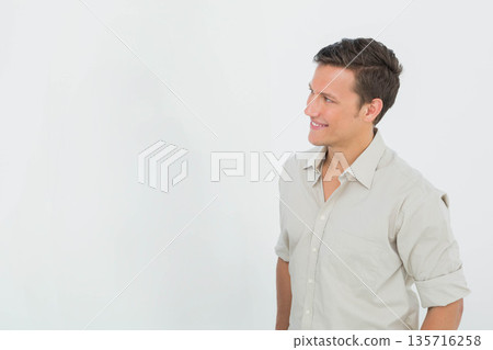 Man standing facing right, looking off-frame in studio wearing beige button-up shirt, copy space 135716258