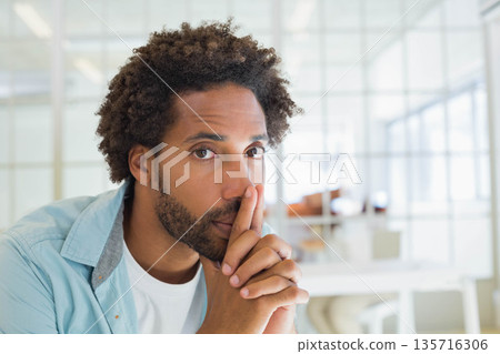 African American man wearing shirt, leaning in, holding finger near lips in office glass partition African American man wearing shirt, leaning in, holding finger near lips in office glass partition 135716306