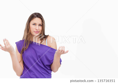Female standing and shrugging puzzled in studio wearing purple off-shoulder top, visible bra strap Female standing and shrugging puzzled in studio wearing purple off-shoulder top, visible bra strap 135716351