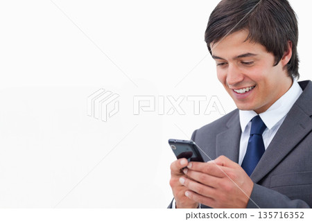 Man in 20s wearing suit and tie holding smartphone, smiling looking down in studio, copy space Man in 20s wearing suit and tie holding smartphone, smiling looking down in studio, copy space 135716352