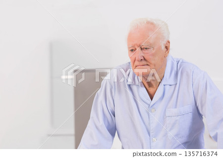 Senior man leaning on bedside, looking down in bedroom, wearing light blue pajama top, copy space Senior man leaning on bedside, looking down in bedroom, wearing light blue pajama top, copy space 135716374