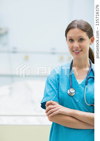 Female nurse standing arms crossed by patient bed in turquoise scrubs and stethoscope, copy space Female nurse standing arms crossed by patient bed in turquoise scrubs and stethoscope, copy space 135716376