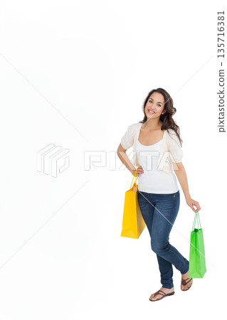 Woman posing on right in studio wearing tank top jeans holding yellow-green paper bags, copy space 135716381