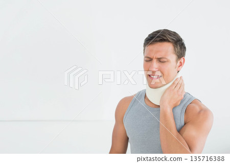 Male standing right by white wall, touching neck, wearing gray tank top and brace, copy space Male standing right by white wall, touching neck, wearing gray tank top and brace, copy space 135716388