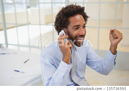 African American man wearing blue shirt and tie sitting at white desk, holding smartphone, papers African American man wearing blue shirt and tie sitting at white desk, holding smartphone, papers 135716393