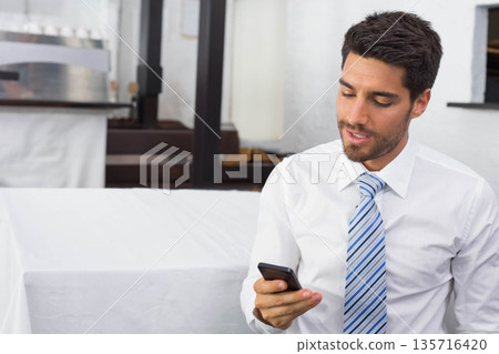 Adult man wearing white shirt, striped tie sitting on bench using smartphone at cafe, copy space 135716420