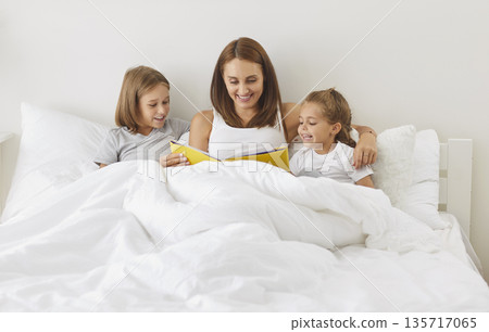 Happy family reading lying in bed, happy mother parent, cute small kids laughing together, children  135717065