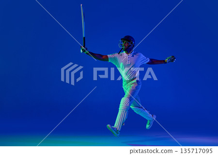 Cricket player jumping with bat after play in blue studio background Cricket player jumping with bat after play in blue studio background 135717095