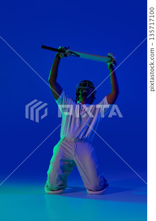 Cricket batsman kneeling upward bat position under blue studio light. Cricket batsman kneeling upward bat position under blue studio light. 135717100