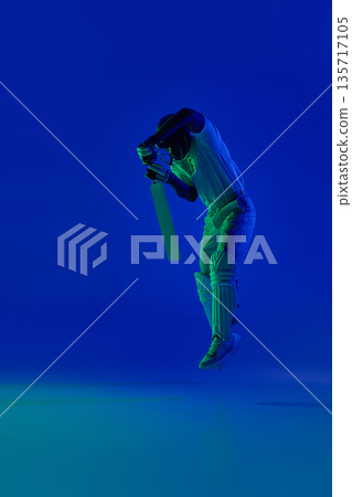 Cricket batsman airborne defensive technique under blue studio light. 135717105