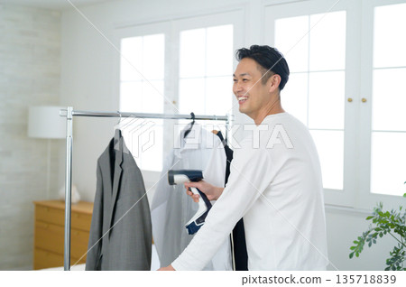 Man steam ironing his suit jacket at home 135718839