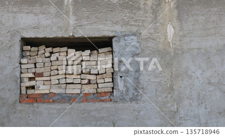 a fragment of a concrete building wall with a window opening on the left, with stacks of used bricks stacked on the interior windowsill, a building in poor condition or in a dilapidated state a fragment of a concrete building wall with a window opening on the left, with stacks of used bricks stacked on the interior windowsill, a building in poor condition or in a dilapidated state 135718946