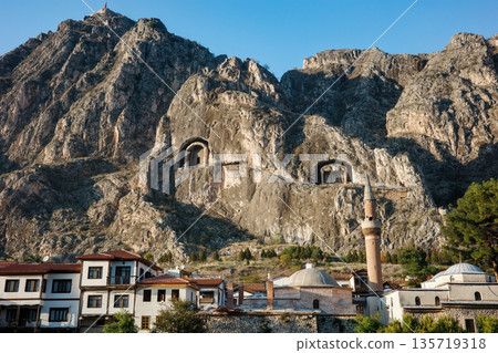 Ancient rock-cut tombs carved in cliff face above Amasya city with traditional Ottoman houses, mosque with minaret below in valley, heritage and historical architecture concept Ancient rock-cut tombs carved in cliff face above Amasya city with traditional Ottoman houses, mosque with minaret below in valley, heritage and historical architecture concept 135719318
