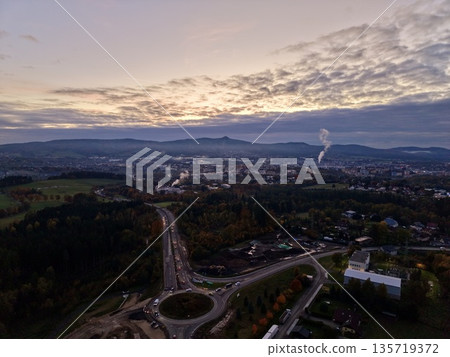 aerial view of evening city junction featuring converging roads and distant industrial emission aerial view of evening city junction featuring converging roads and distant industrial emission 135719372
