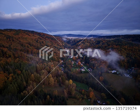 quiet village beneath misty hills, idyllic hamlet nestled under cloudcovered forested hill at dusk quiet village beneath misty hills, idyllic hamlet nestled under cloudcovered forested hill at dusk 135719374