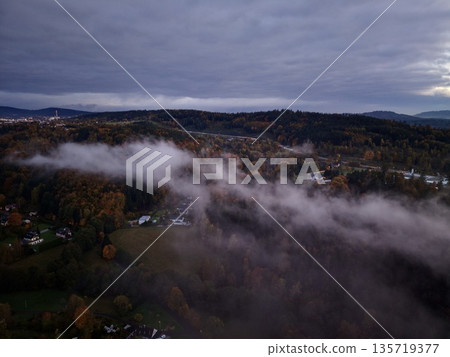 misty landscape view, foggy valley with muted hues, thick fog cascading over rooftops and trees 135719377