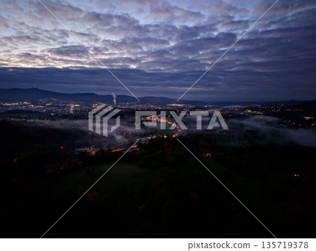 dark urban landscape at night, drone captures moody nighttime city with fog and lights contrast 135719378