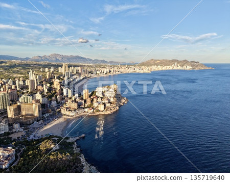 coastal skyline sunrise, beachfront cityscape with morning glow, highrise harbor city illuminated at dawn 135719640