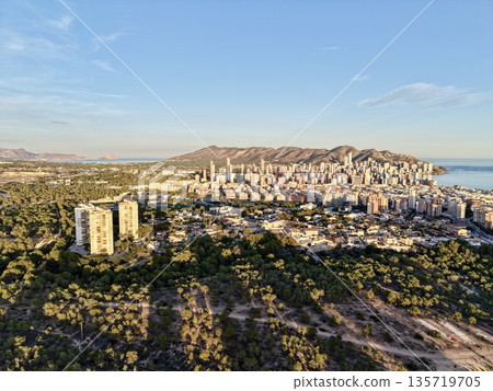 photograph depicting mountain valley flowing into sea with twilight shadows and distant city silhouettes 135719705