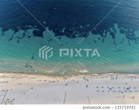 vibrant seaside with visitors, idyllic shoreline captured with lively sunbathers and clear water 135719781