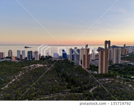 twilight cityscape near ocean, evening cityscape with illuminated towers and peaceful waterscape twilight cityscape near ocean, evening cityscape with illuminated towers and peaceful waterscape 135719792