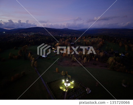 calm rural landscape featuring lit cottage amid shadowed meadows and wooded hills at twilight 135720066